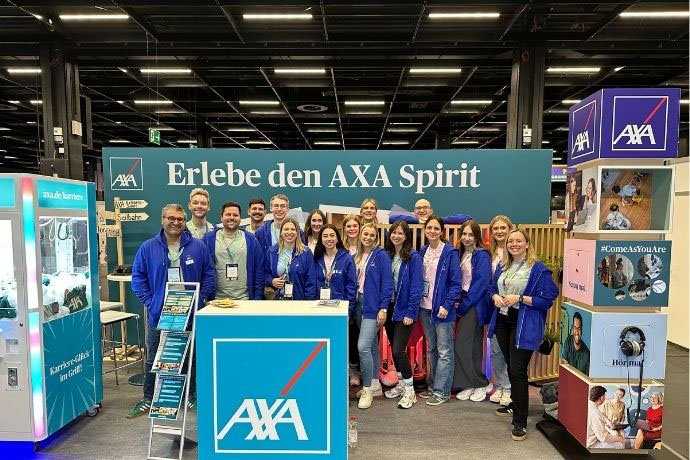 AXA Team steht lächelnd vor eigenem Messestand auf dem Absolventenkongress in Köln