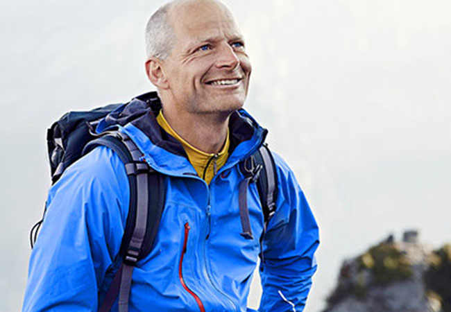 Mann mit Rucksack und Outdoor-Kleidung steht in bergiger Landschaft und blickt nach oben