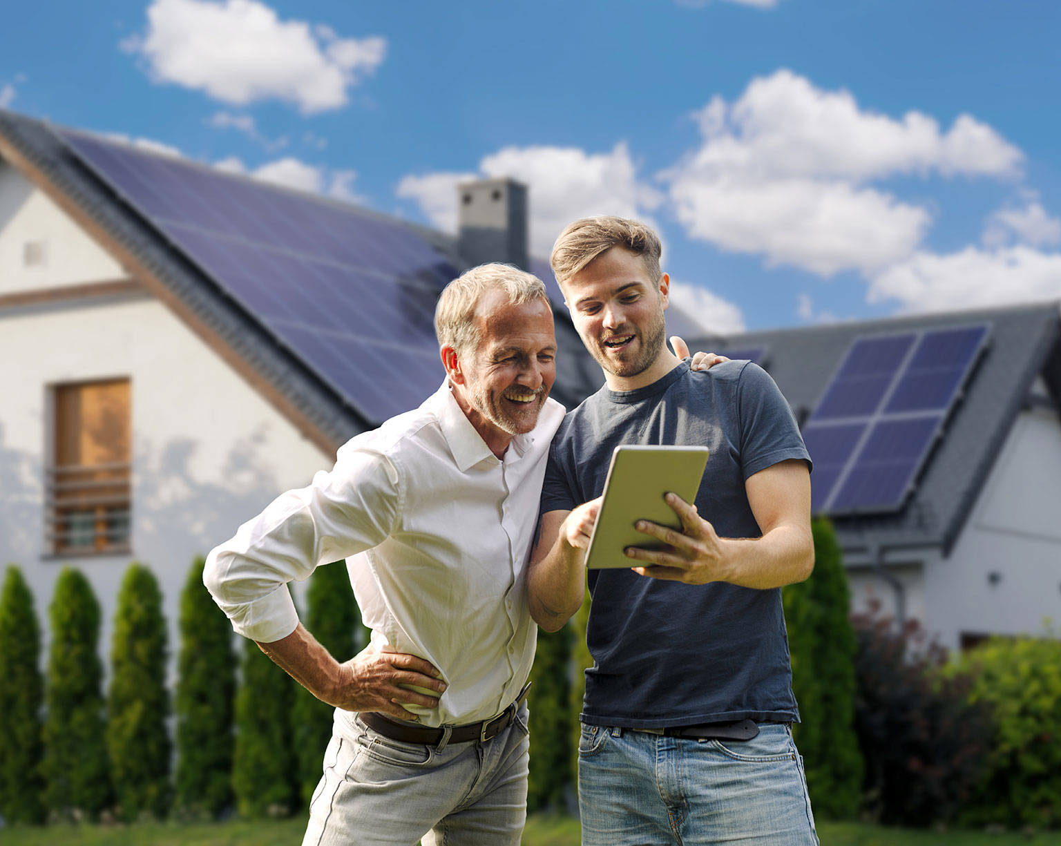 Vor einem Haus mit Solarzellen schauen zwei Männer auf ein Tablet