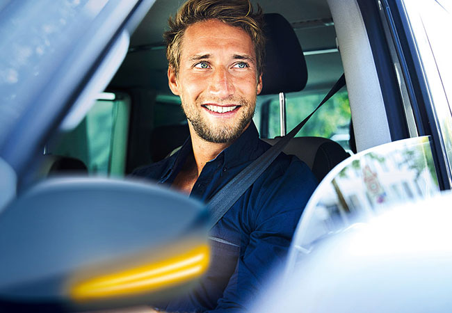 Junger Mann fährt Auto mit geöffnetem Fenster und lächelt.