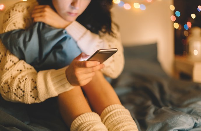 Junges Mädchen schaut auf ihr Smartphone und versucht ihre Einsamkeit damit zu kompensieren