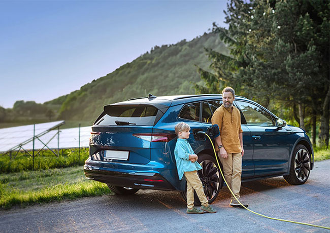 Vater steht mit seinem Sohn vor dem Auto, das elektrisch geladen wird.