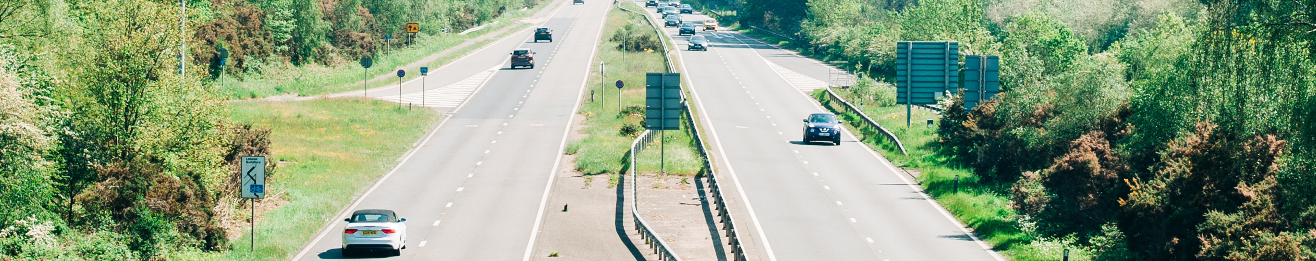 Versicherung für Ihren Smart abschließen Mehrere Autos fahren auf einer mehrspurigen Schnellstraße durch eine grüne, bewaldete Landschaft.