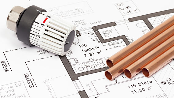 Thermostatkopf und mehrere Kupferrohre liegen auf einem technischen Gebäudegrundriss. Die Zeichnung zeigt Raumaufteilungen und Installationsbereiche für Wasser, Elektro und Heizung.