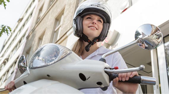 Junge Frau mit Helm sitzt auf einem weißen Roller