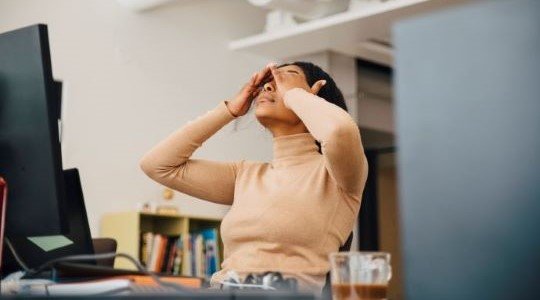 Frau sitzt mit den Händen vor dem Gesicht am Schreibtisch
