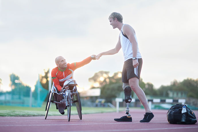 Zwei Parasportler geben sich auf einem Sportplatz die Hand