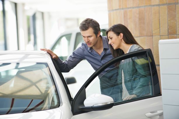 Ein Mann und eine Frau betrachten gemeinsam ein weißes Auto mit geöffneter Fahrertür.
