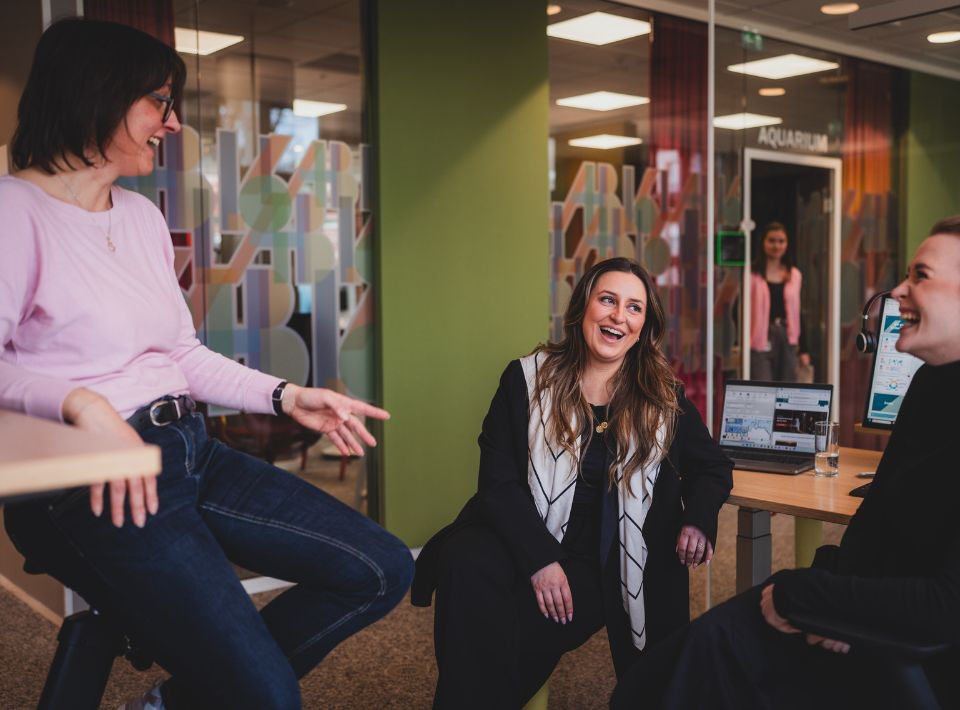 Kolleginnen von AXA sitzen in einem Büro und lachen gemeinsam
