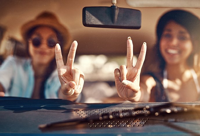 Zwei junge Frauen zeigen Victory-Handzeichen im Auto