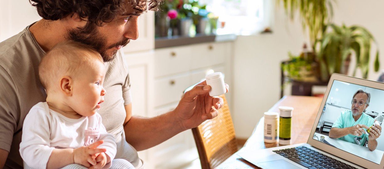 Junger Mann mit Baby auf dem Schoss spricht mit dem Online-Arzt